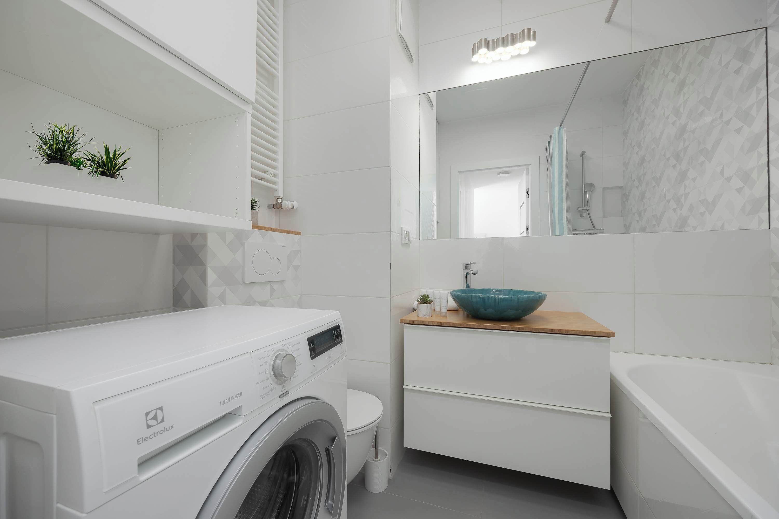 Une salle de bain moderne équipée d’un lave-linge, d’un lavabo avec un receveur bleu et d’un miroir.