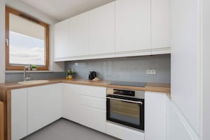 Une cuisine moderne avec des meubles blancs, un plan de travail en bois, un four encastré et une fenêtre au-dessus de l’évier.