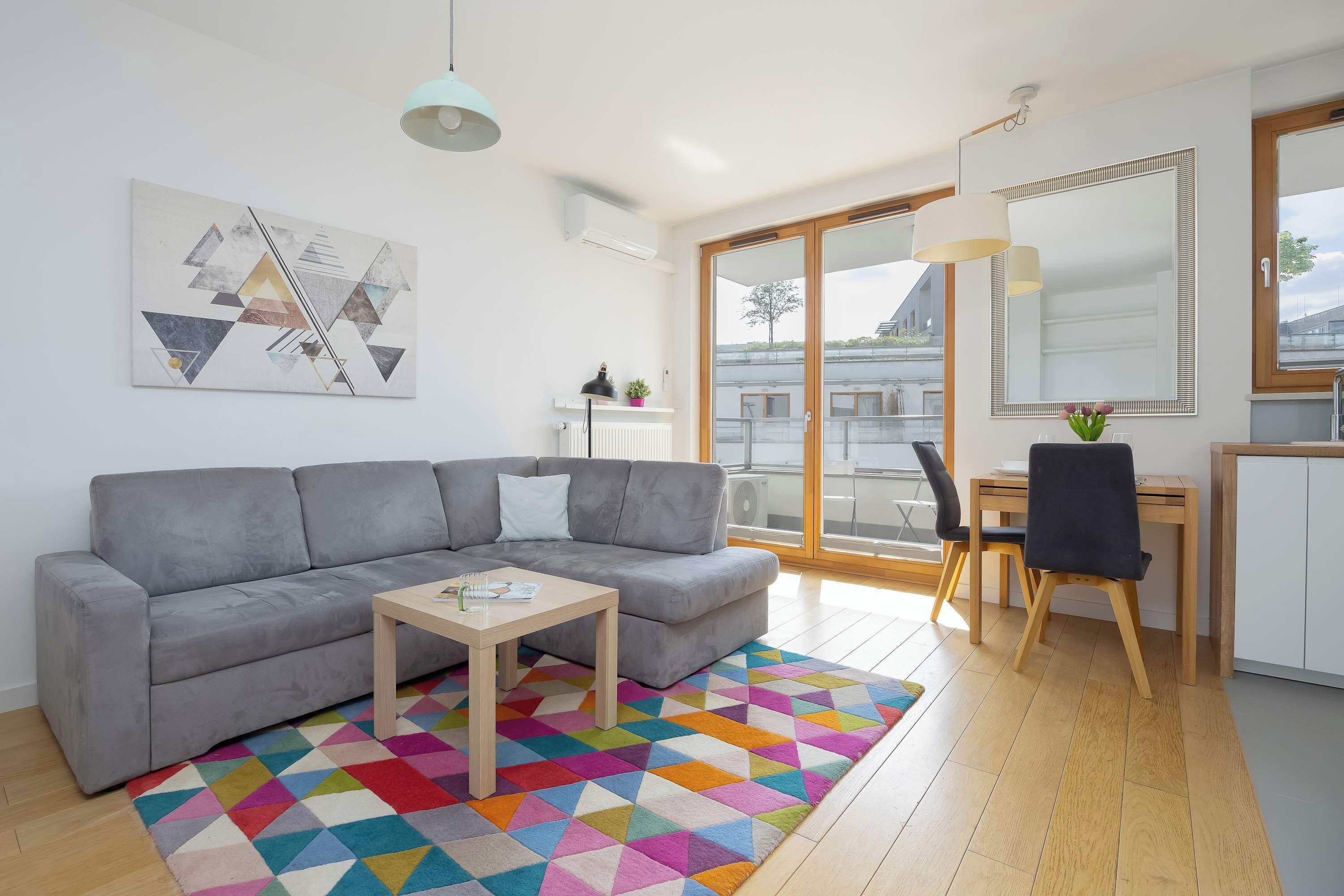 Un salon moderne avec un canapé gris, une table basse en bois et un tapis géométrique aux couleurs vives.