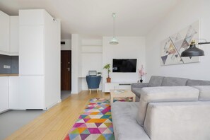 A modern living room with a grey sofa, a coffee table, a TV, and a colorful geometric rug. - Klimatisiertes Apartment | Parkplatz | Warschau-Wola (Warszawa)
