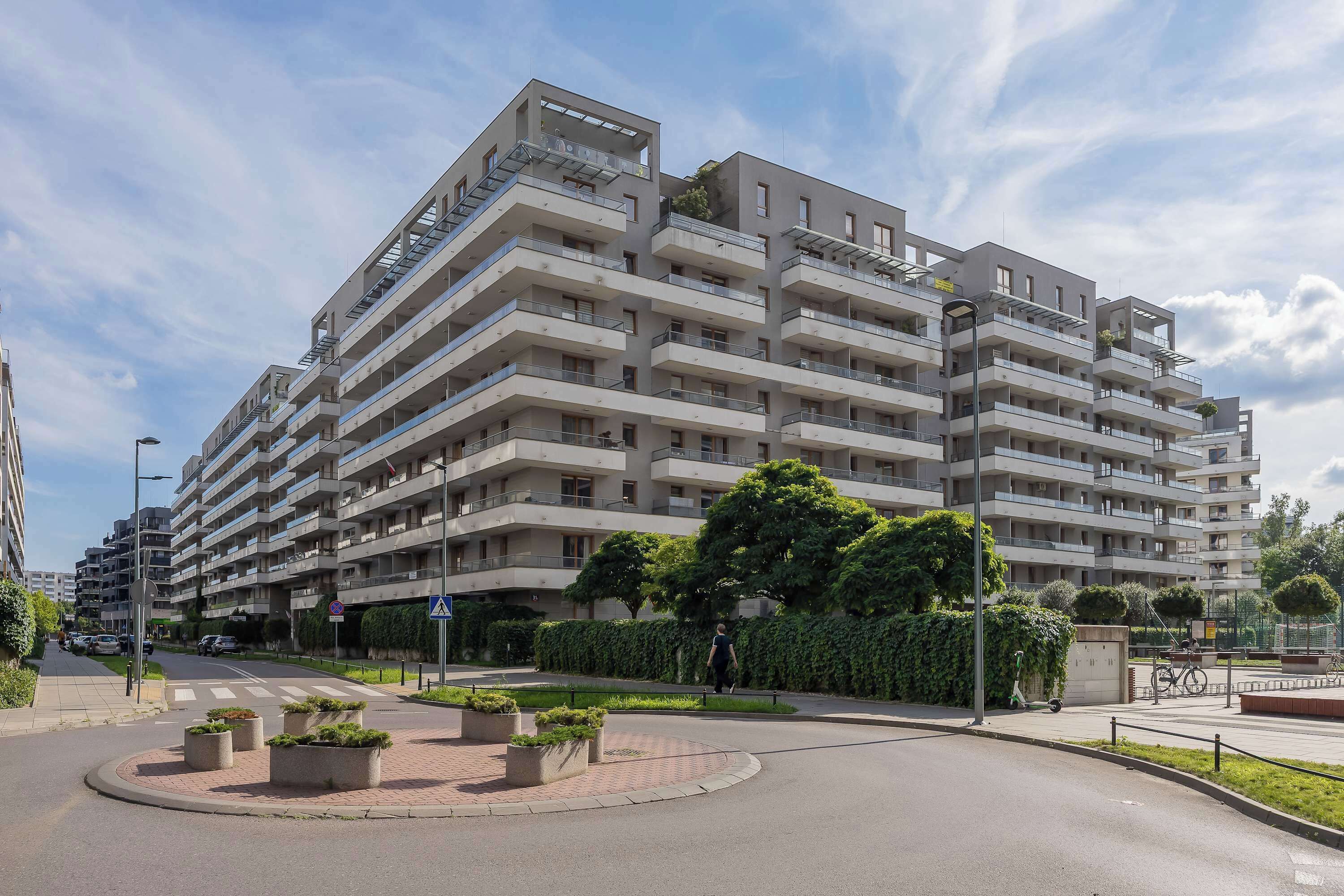 Un edificio residencial de varios pisos con balcones, un paso de peatones y una glorieta.