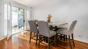Un coin repas comprenant une table et quatre chaises, un vase avec des fleurs et une porte-fenêtre coulissante donnant sur un espace extérieur.