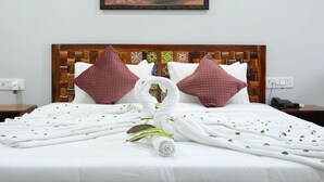 A hotel room with a bed, pillows, a towel, a painting on the wall, and a wooden headboard. - Sai Dhara Resort (Kasrawad)