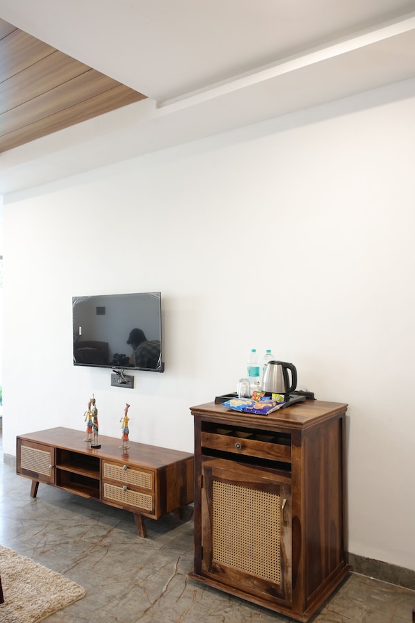 A living room with a flat-screen TV mounted on the wall, a wooden cabinet with drawers, and a wicker basket. - Sai Dhara Resort (Kasrawad)