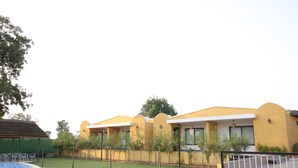 A modern building with a yellow facade, a swimming pool, and a well-maintained lawn. - Sai Dhara Resort (Kasrawad)