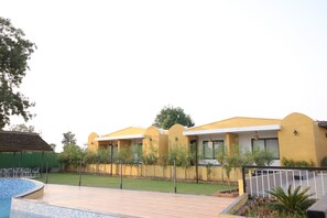 A modern building with a yellow facade, a swimming pool, and a well-maintained lawn.