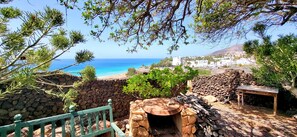 Un mur de pedra, una taula de fusta i vista al mar i edificis.