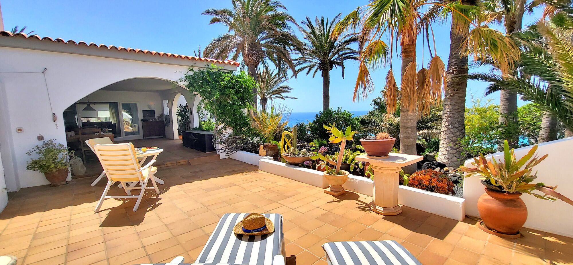 A patio with a table and chairs, potted plants, and a view of the sea.