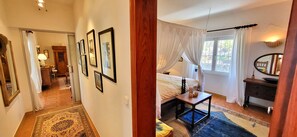 A bedroom with a bed, a bedside table, a mirror, and a window with curtains.