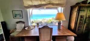 Una habitació amb taula de fusta, una làmpada, un barret i vista a l'oceà.