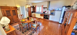 Una cuina amb armaris de fusta, una taula de dinar amb cadires, un refrigerador i un microones.