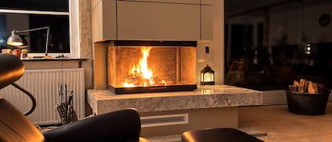 A modern living room with a fireplace, a sofa, a coffee table, and a view of the outside.