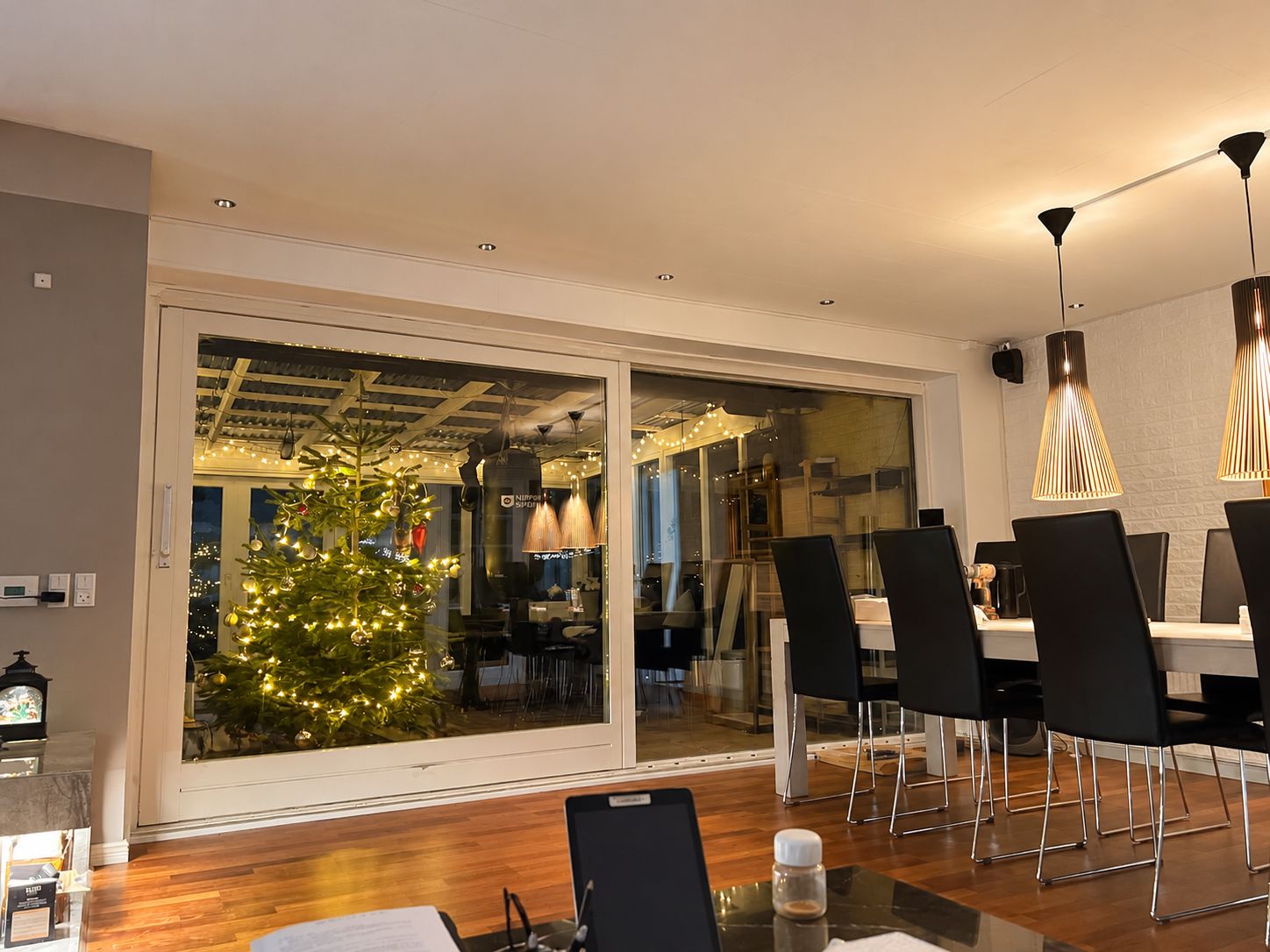 Un'area pranzo moderna con una porta in vetro che dà su una cucina, un piccolo albero di Natale e mobili contemporanei.