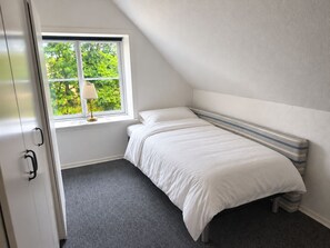 A bedroom with a single bed, a window with a view of greenery, and a closed door.