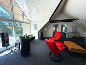 A modern room with a large window, a red chair, a black speaker, and a wooden table. - Farmhouse in Bælum - rural tranquility 20 minutes from Aalborg (Bælum)
