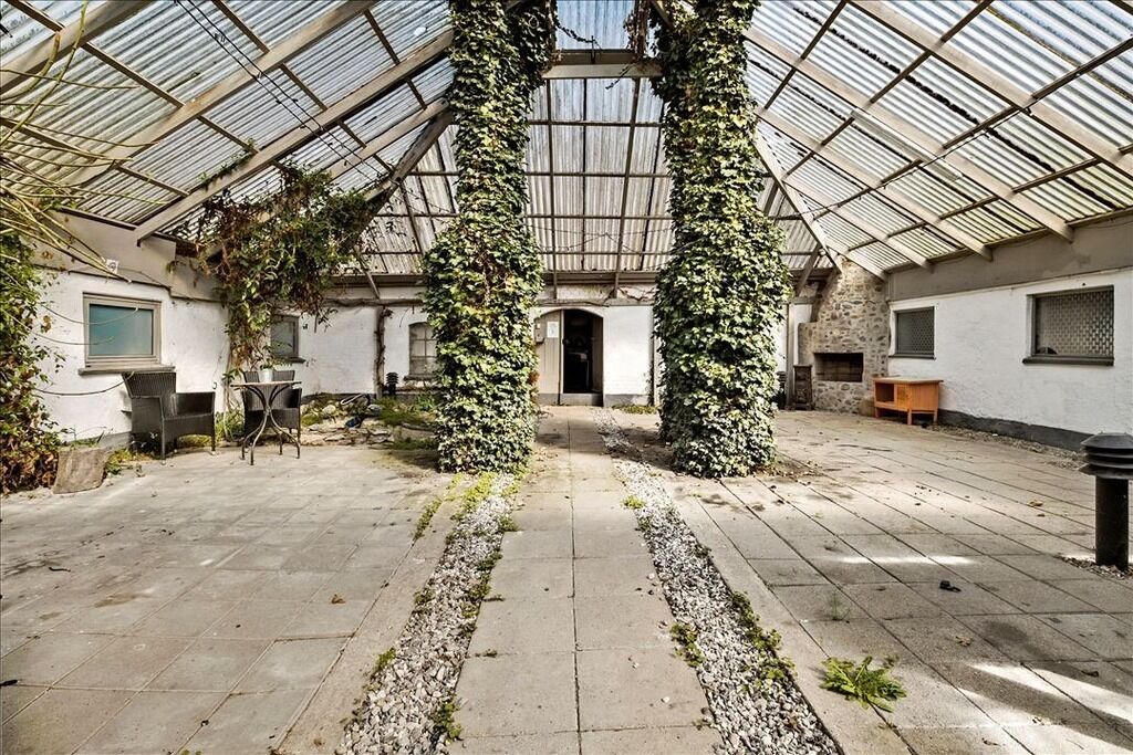A greenhouse with a glass roof, stone walls, and a central pathway.