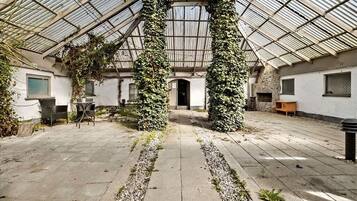 A greenhouse with a glass roof, stone walls, and a central pathway.