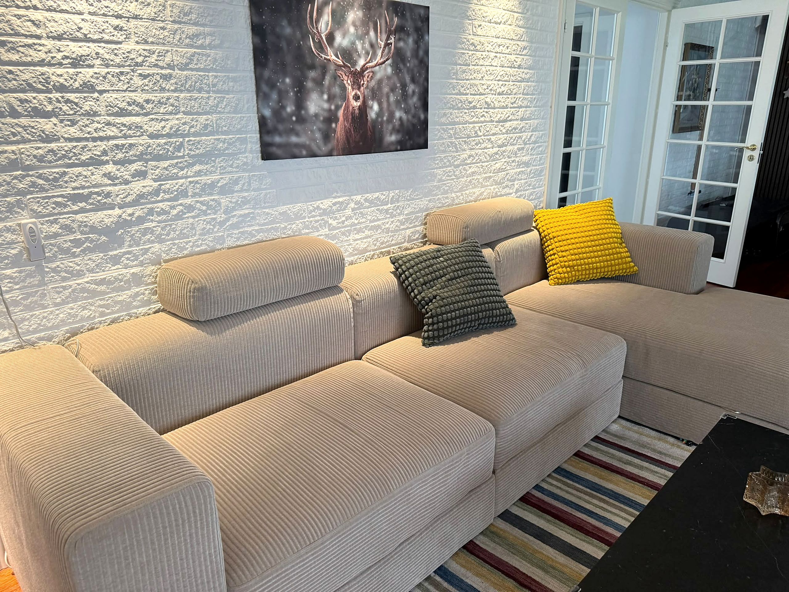 Un canapé beige avec deux coussins, une table basse noire et un tapis à rayures.