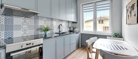 A modern kitchen with grey cabinets, a patterned backsplash, and a window with blinds.