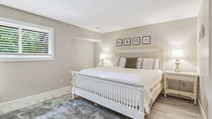 A bedroom with a bed, bedside tables, a window with blinds, and wall-mounted artwork. - Sunset Rentals | Greens 170 Dog Friendly! (Hilton Head Island)