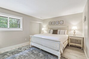 Ein Schlafzimmer mit einem Bett, Nachttischen, einem Fenster mit Jalousien und Wandbildern.