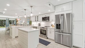 A modern kitchen with white cabinetry, stainless steel appliances, pendant lighting, and a view of the outdoors. - Sunset Rentals | Greens 170 Dog Friendly! (Hilton Head Island)