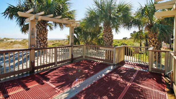 A covered outdoor area with a metal floor, palm trees, and a wooden pergola. - Sunset Rentals | Greens 170 Dog Friendly! (Hilton Head Island)