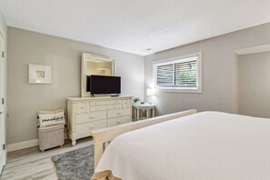 A bedroom with a bed, dresser, television, and window with blinds. - Sunset Rentals | Greens 170 Dog Friendly! (Hilton Head Island)