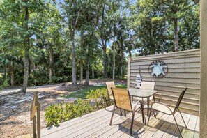An outdoor deck with a table and chairs, surrounded by trees. - Sunset Rentals | Greens 170 Dog Friendly! (Hilton Head Island)