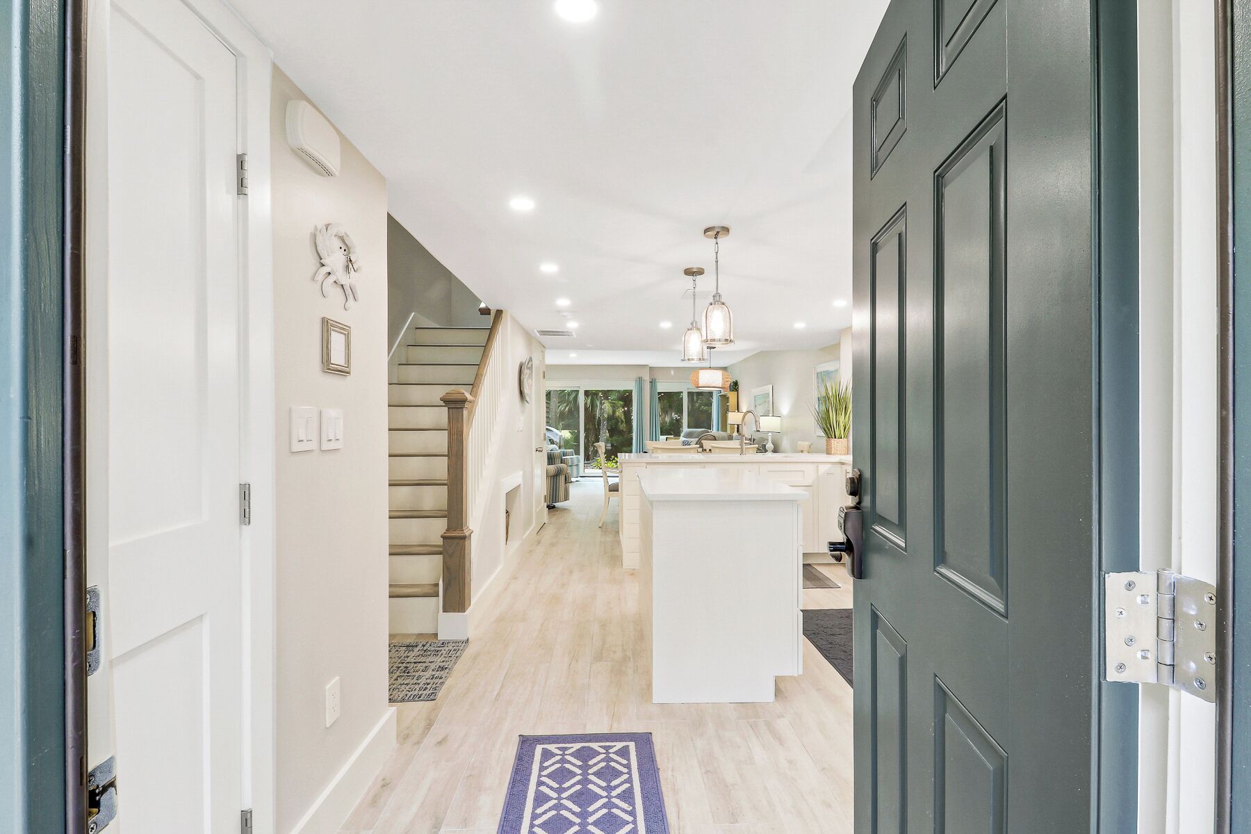 A modern kitchen with a central island, a staircase leading to another level, and a hallway with a door on the right.