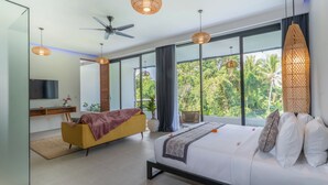 A modern bedroom with a large bed, a sofa, a TV, and a balcony with a view of trees.