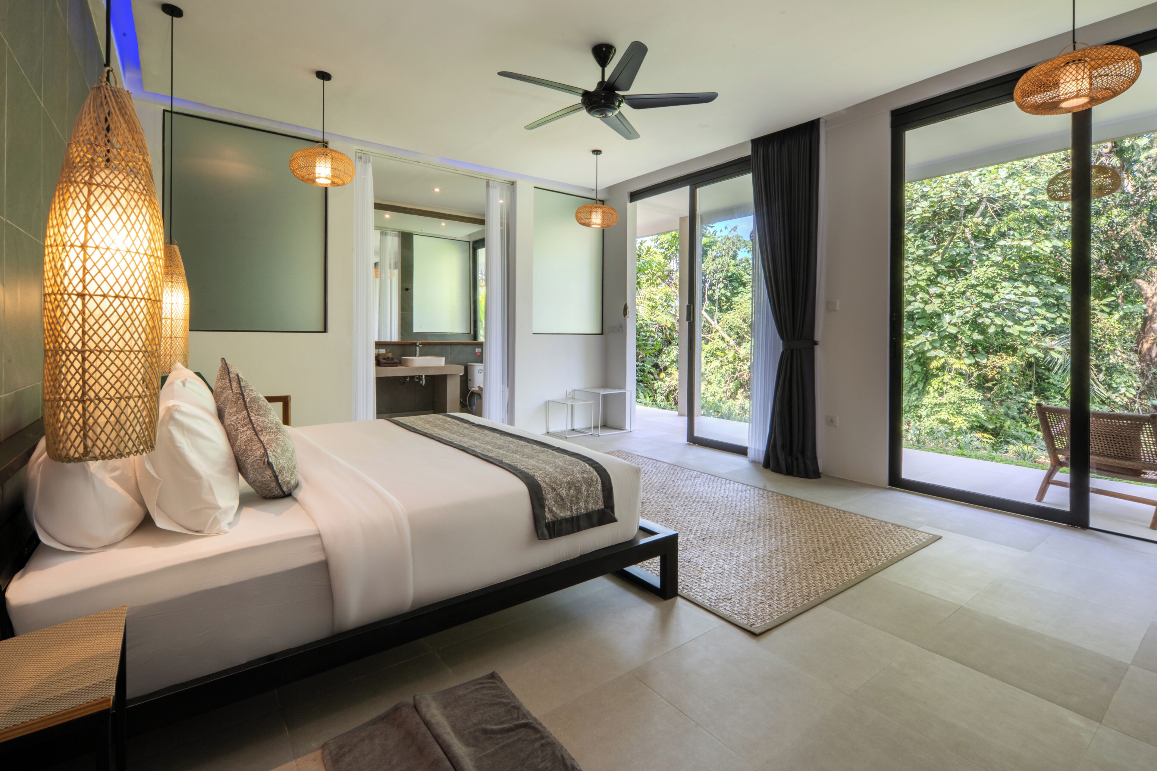 A modern bedroom with a bed, bedside lamps, a ceiling fan, and a view of the outdoors.