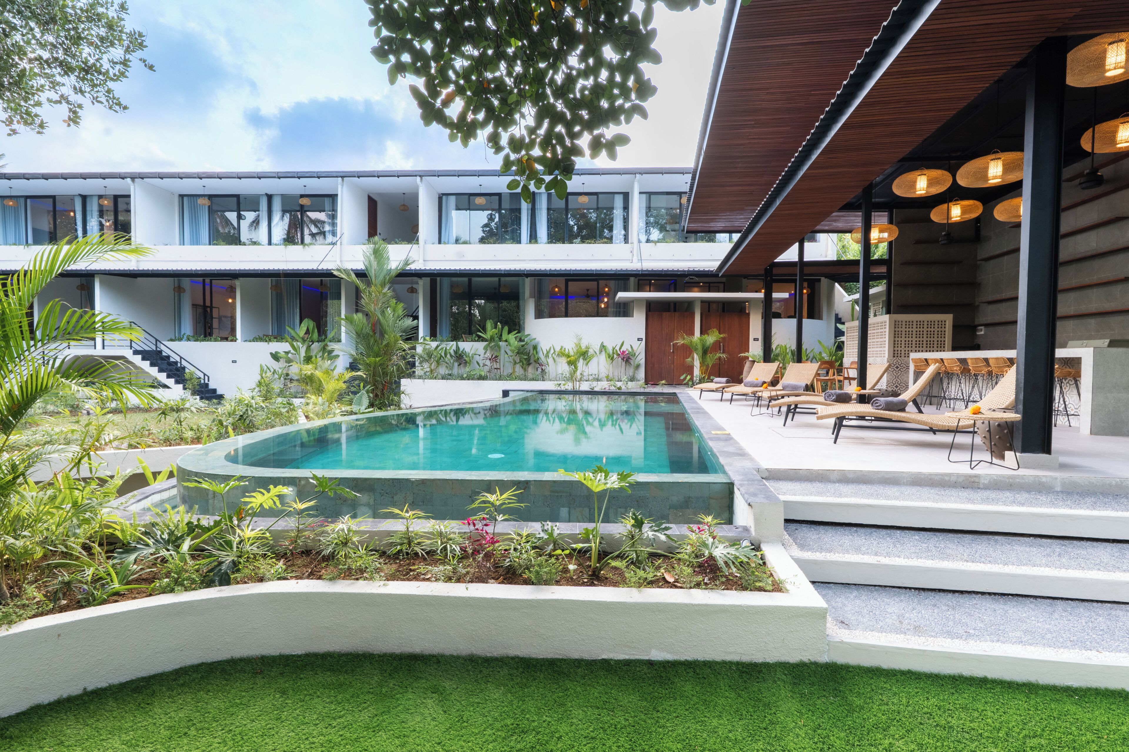 A modern building with a swimming pool, outdoor seating, and lush greenery.