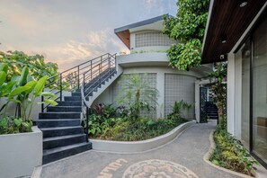 Un bâtiment moderne doté d’un escalier menant à un balcon, le tout entouré d’une végétation luxuriante.
