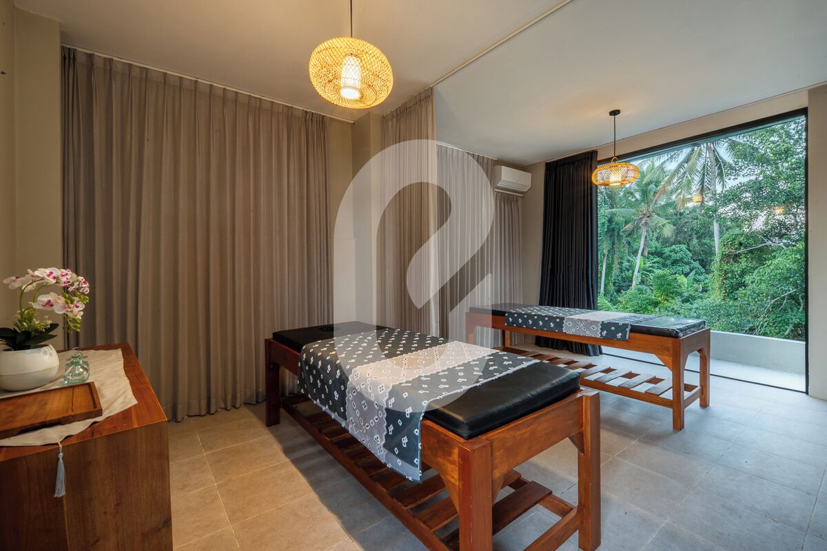 A room with a bed, a desk, a chair, a hanging light fixture, and a view of greenery outside.