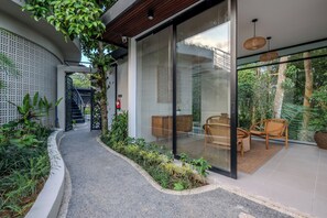 Una casa moderna con puerta de entrada de vidrio, una escalera que conduce al piso superior y un área de estar con muebles de mimbre.