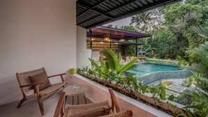 A patio with wicker furniture, a small table, and a pool surrounded by lush greenery.