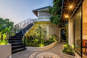 Un edificio moderno con una escalera que lleva a un balcón, rodeado de abundante vegetación.