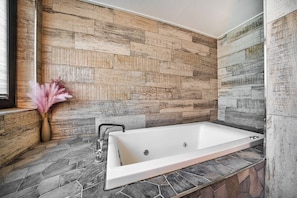 A bathroom with a stone wall, a white bathtub, and a vase with pink flowers. - Hotel Parkview (Seoul)