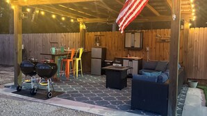 An outdoor patio with a wooden pergola, string lights, a grill, outdoor furniture, and an American flag. - Waterfront Getaway with Campfire Fishing Kayaking Biking Near Beaches & MS (Coden)