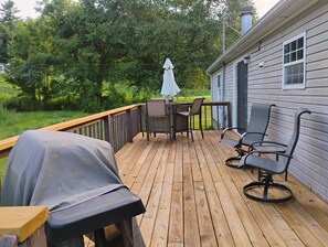 Een houten terras met buitenmeubilair, waaronder een tafel, stoelen en een barbecue.