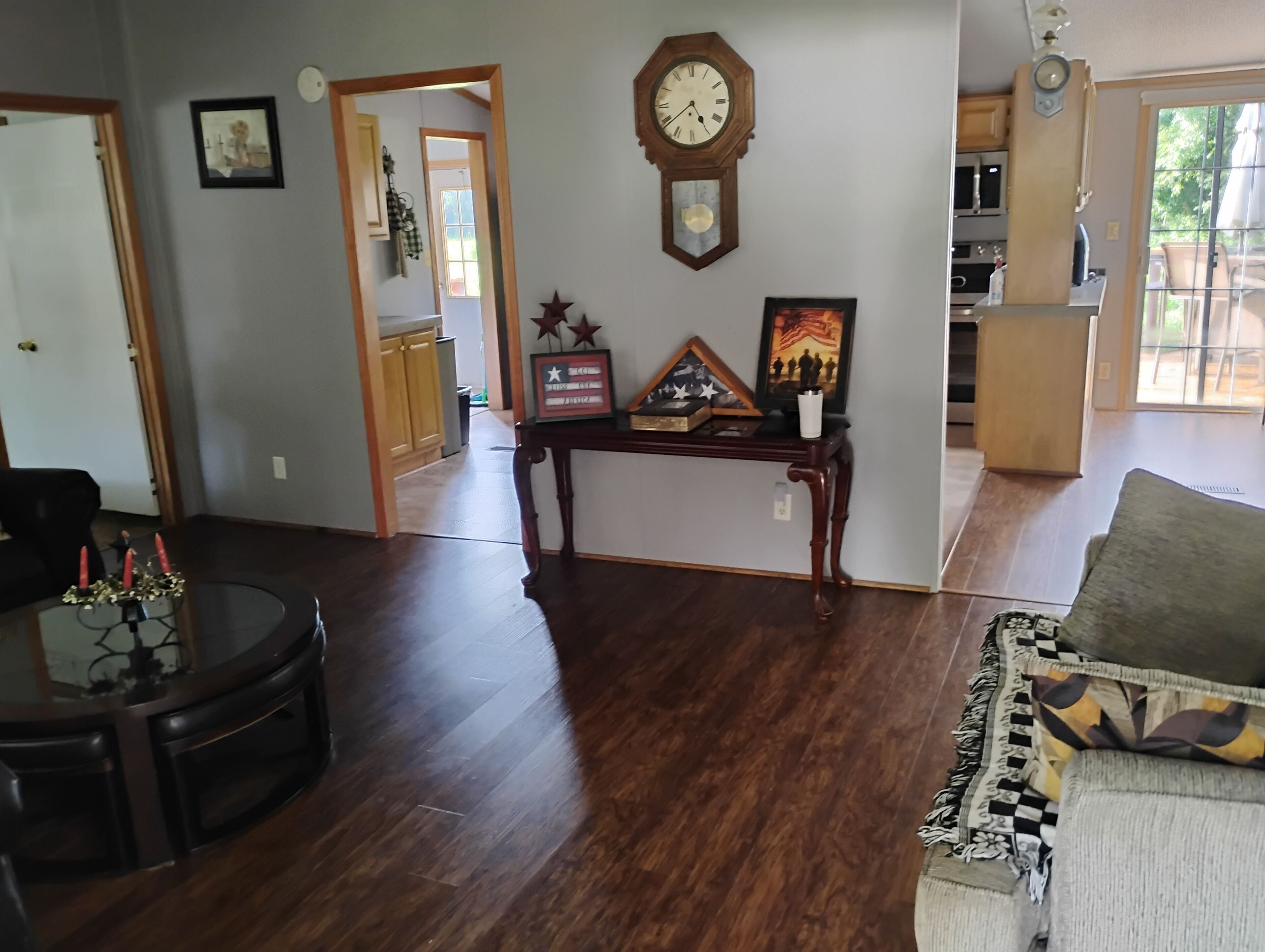 Una sala de estar con piso de madera, una mesa de comedor con velas, un sofá, un reloj y una cocina al fondo.