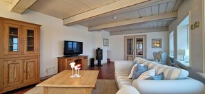 A living room with a wooden cabinet, a television, a table with candles, and a striped sofa. - Thatched cottage near the North Sea (Dagebüll)
