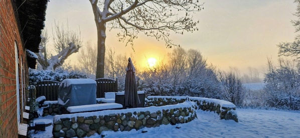 A snow-covered outdoor area with a stone wall, a bench, and a patio umbrella. - Thatched cottage near the North Sea (Dagebüll)