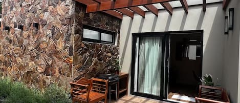 A patio with a stone wall, wooden furniture, and a pergola.