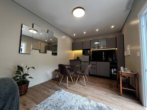 A compact living space with a dining area, kitchenette, and a large mirror on the wall. - Studio Cool! (Gramado)