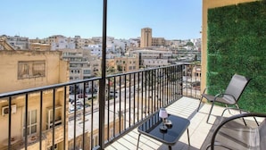 Un balcon donnant sur le paysage urbain, une petite table avec une lampe et une chaise.