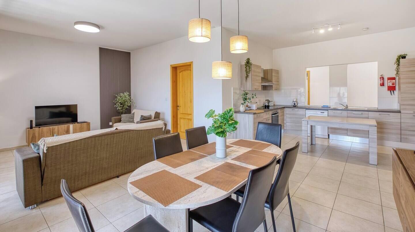 A modern kitchen with a dining area, featuring a central island, pendant lighting, and a television.