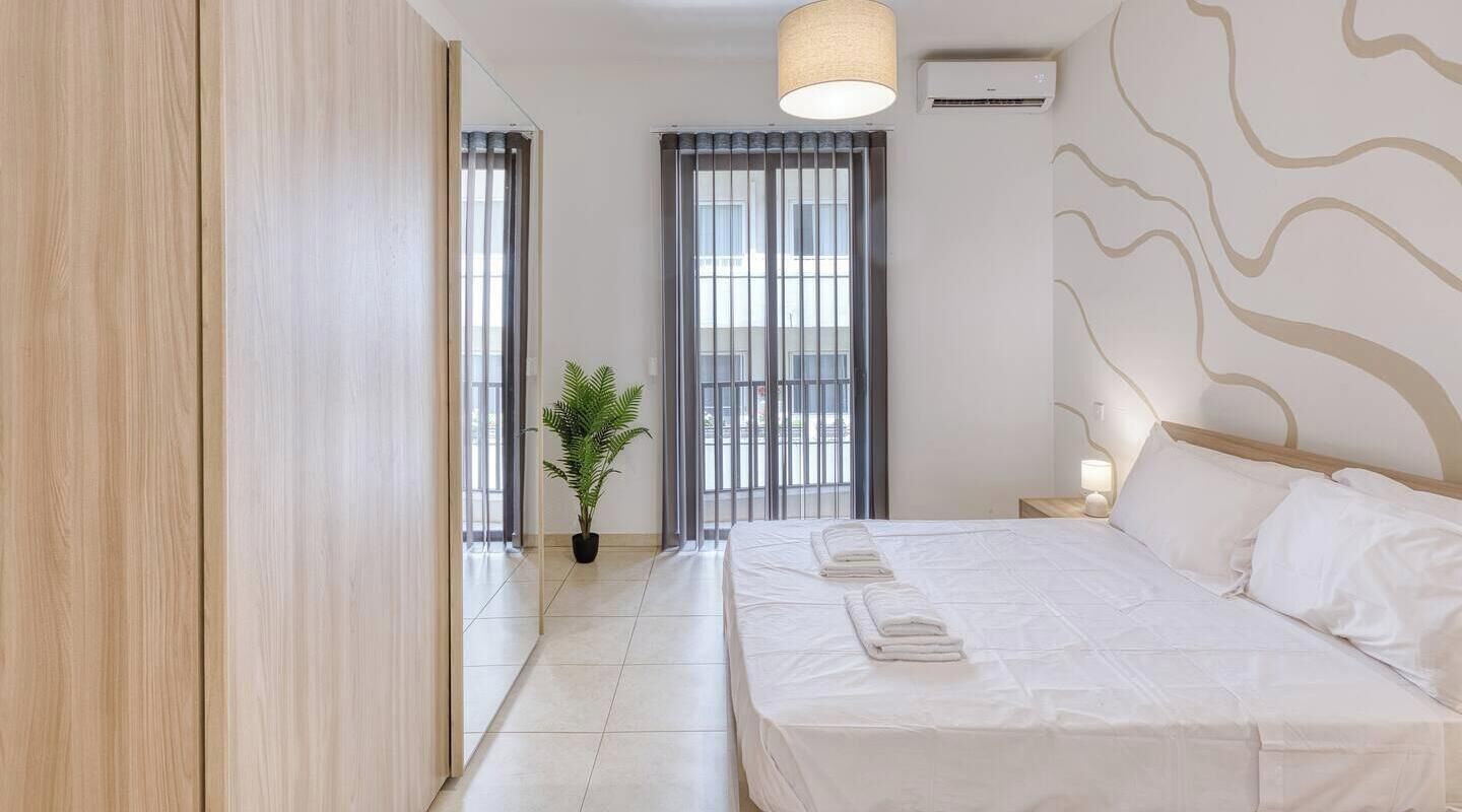 A hotel room with a bed, a nightstand, a potted plant, and a window with curtains.