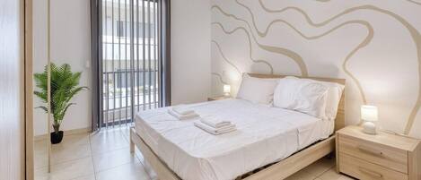 Quarto de hotel com cama, mesa de cabeceira, luminária e um vaso de planta.